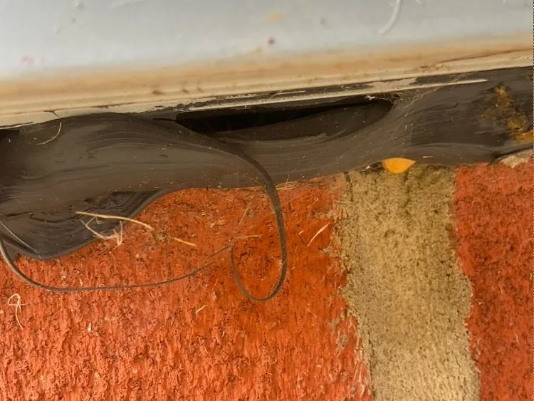 Photo of gaps in the mastic beneath a patio door sill, with a loose strand of mastic hanging down